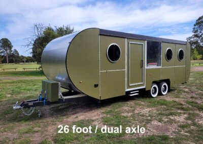 26-foot dual axle caravan with olive green exterior and three round windows, parked outdoors on grass.