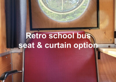 Caravan interior featuring a retro-style school bus seat with a wooden back and dark upholstery, paired with a matching curtain.