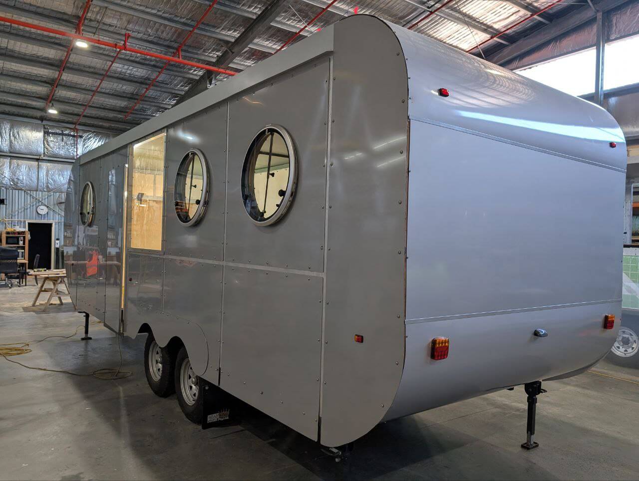 Rear view of a silver Hammervan caravan with Probond cladding, showing the curved back and dual axles in a workshop.