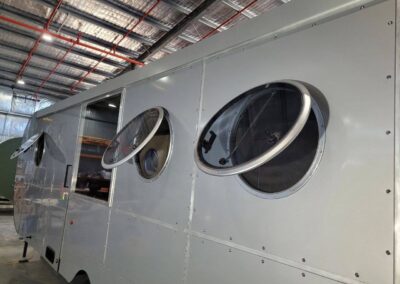 Two large opening porthole windows on the side of a silver caravan, showing the screens and ventilation feature.