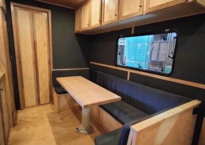 Spacious caravan living area with black upholstered dinette, wooden table, and overhead storage cabinets, showing a modern interior.