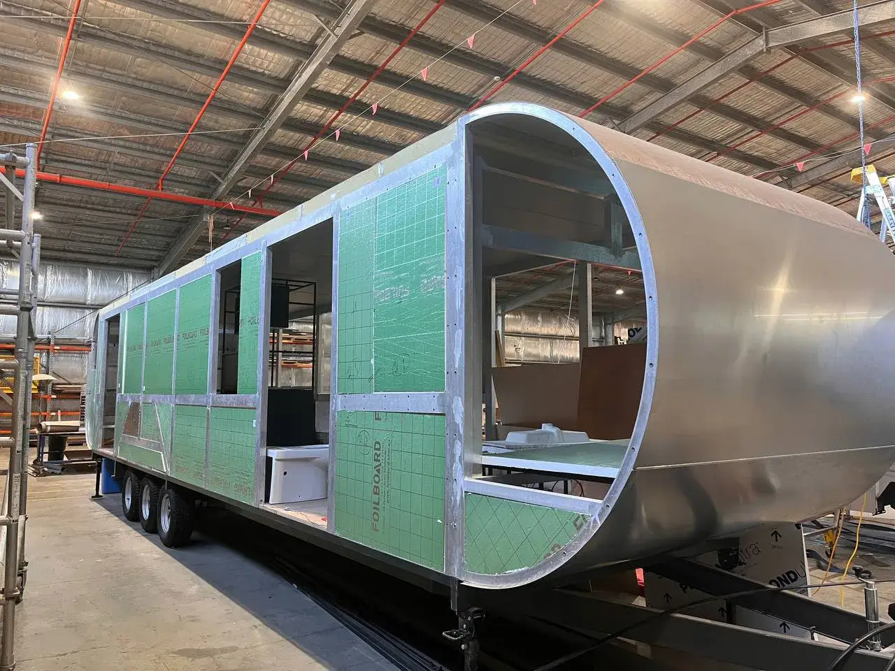 Large 37ft caravan in an early stage of construction, revealing the aluminum frame and green insulation on the exterior.
